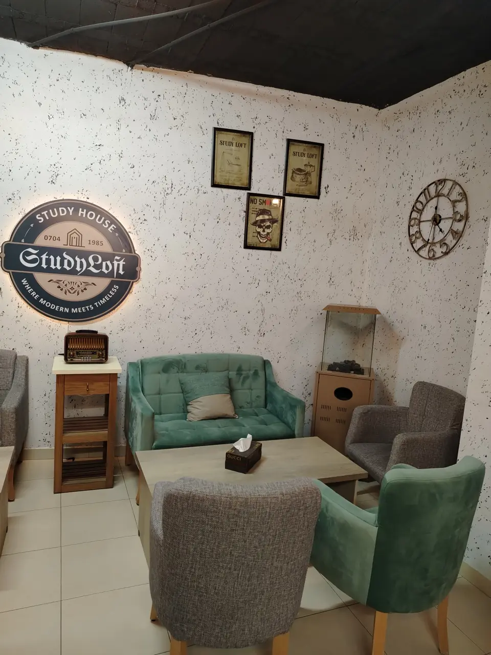 A green armchair, wooden tables, a vintage radio and clock, and the illuminated Study Loft sign